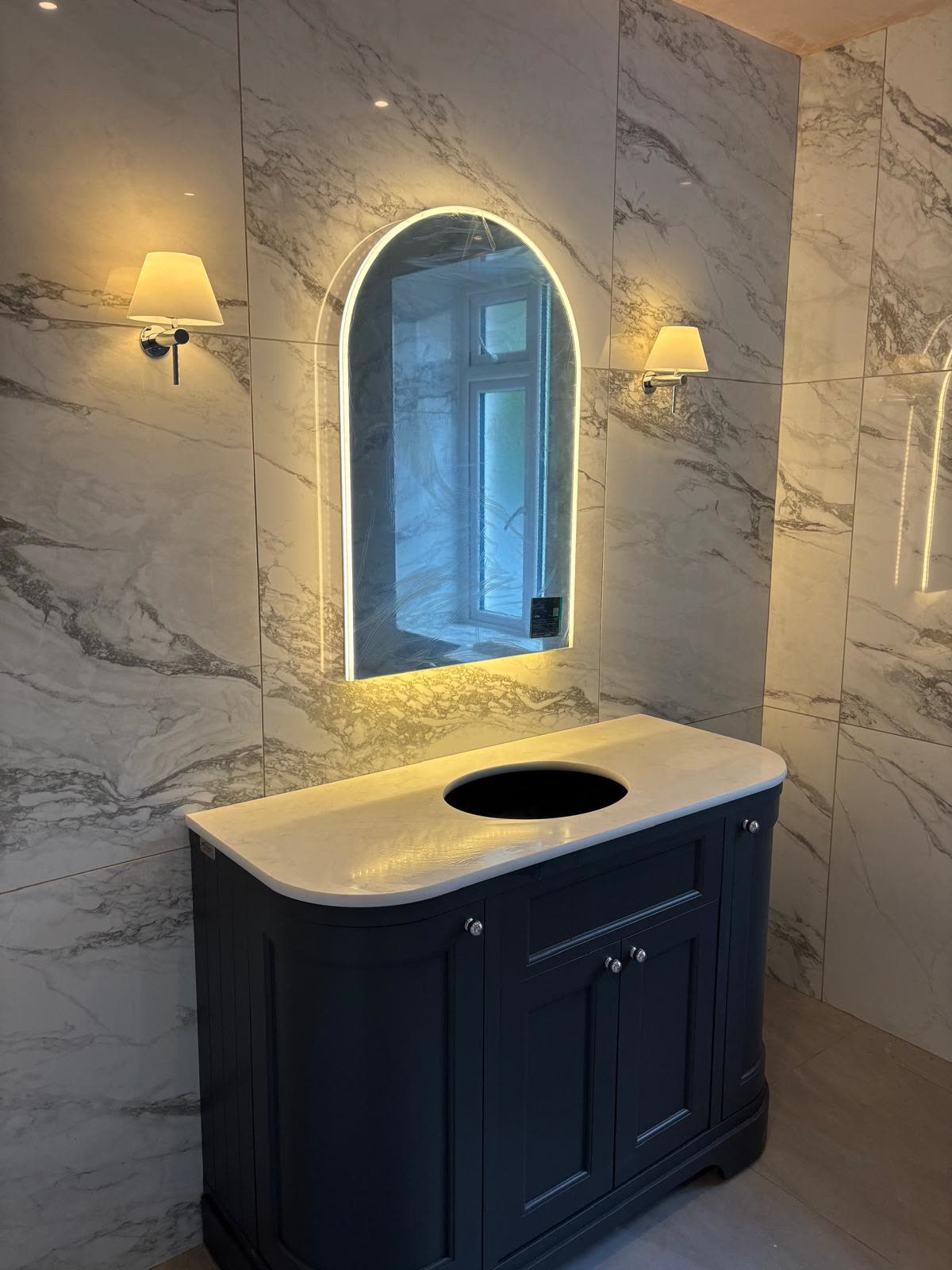 A bathroom with a lit mirror and wall lights fitted by RM Electrical
